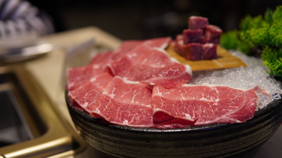 A close-up of thinly sliced beef on ice, showcasing freshness and marbling.