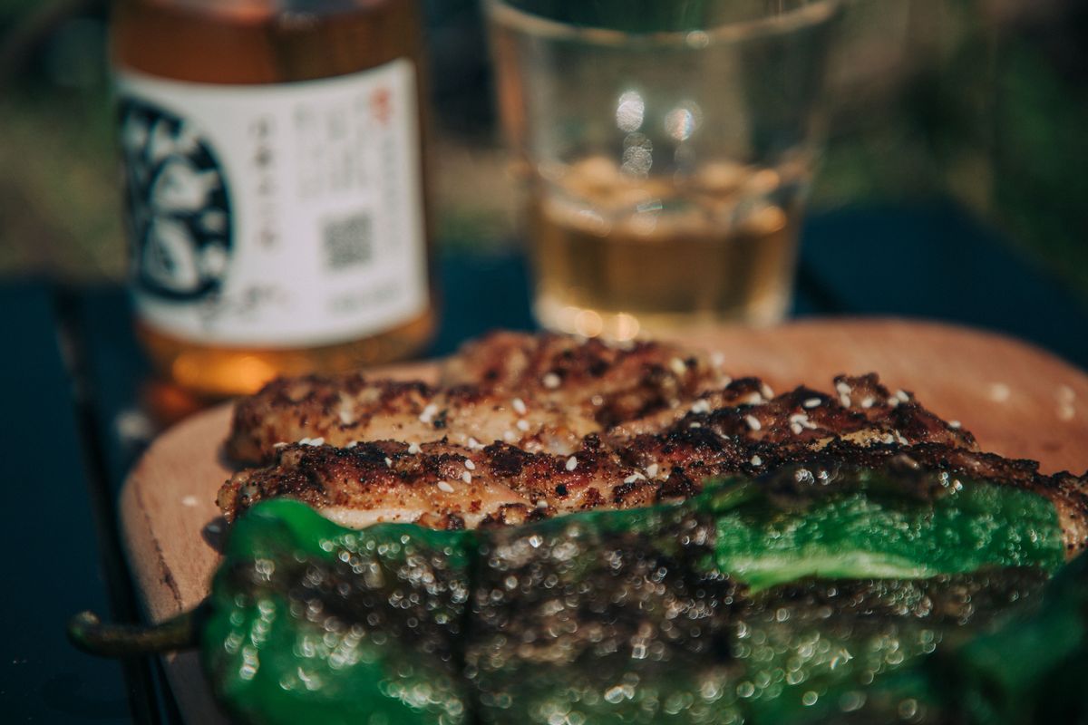 Close-up of grilled meat with a beverage in a relaxed outdoor setting.